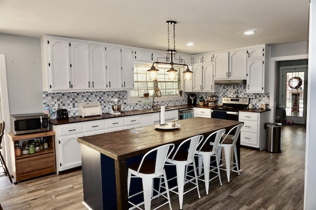 kitchen featuring white cabinetry, stainless steel appliances, wooden counters, a breakfast bar area, and a kitchen island