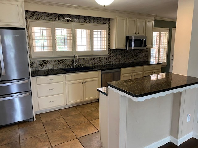 kitchen featuring sink, stainless steel appliances, tile patterned flooring, dark stone counters, and ornamental molding