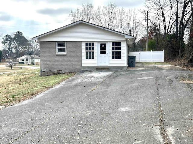 view of front of home with driveway, brick siding, crawl space, and fence