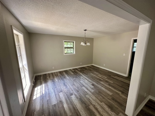 unfurnished dining area with a chandelier, a textured ceiling, and dark wood-type flooring