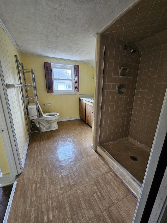 bathroom with vanity, wooden walls, toilet, a textured ceiling, and tiled shower