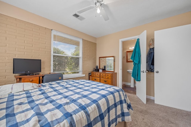 bedroom with ceiling fan, ensuite bathroom, brick wall, and light carpet