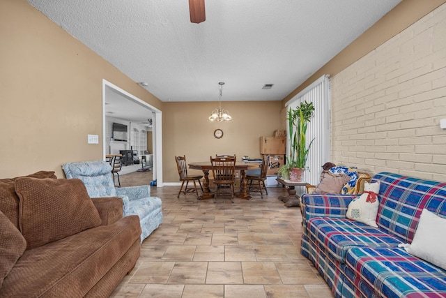 living room featuring a textured ceiling, brick wall, and ceiling fan with notable chandelier