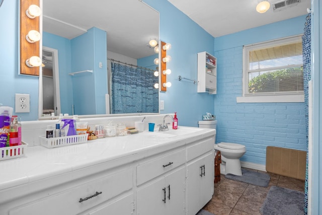 bathroom featuring tile patterned floors, vanity, brick wall, and toilet