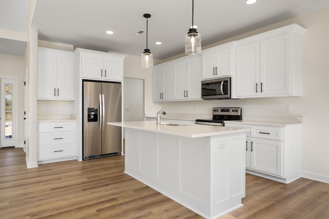 kitchen featuring a center island with sink, stainless steel appliances, decorative light fixtures, white cabinets, and sink