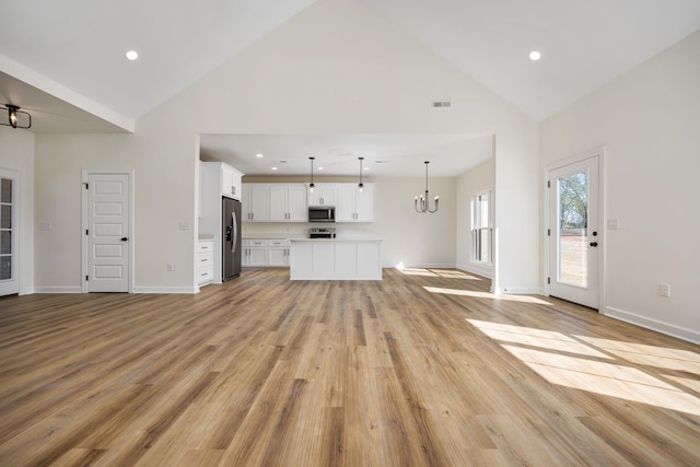 unfurnished living room with light hardwood / wood-style floors, high vaulted ceiling, and a notable chandelier