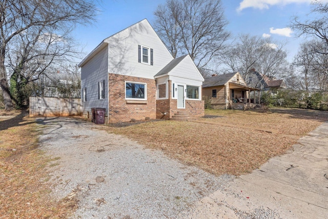 view of front facade featuring driveway, brick siding, and fence