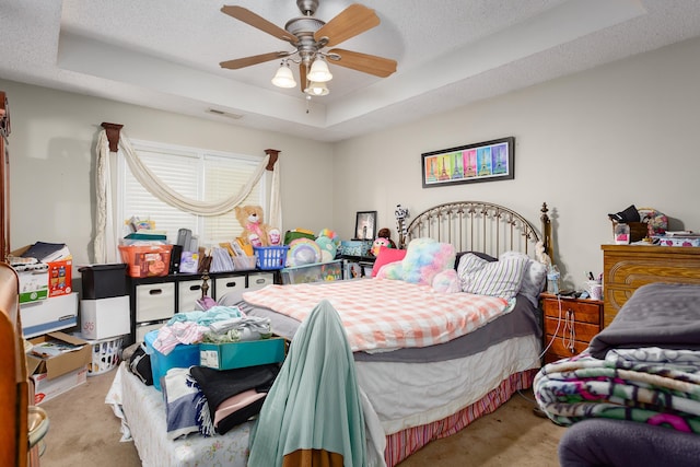 bedroom featuring a textured ceiling, ceiling fan, a raised ceiling, and light carpet