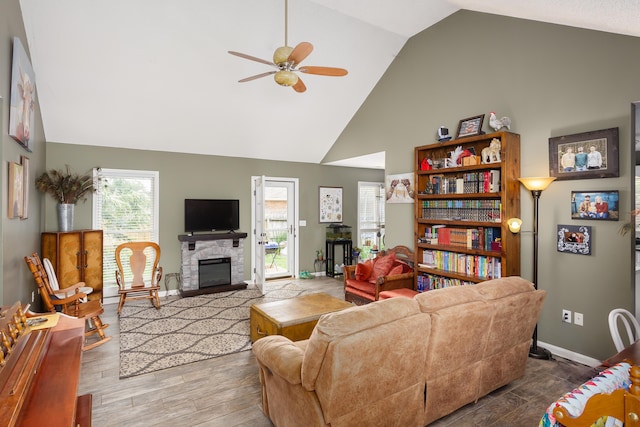 living room featuring hardwood / wood-style floors, ceiling fan, a stone fireplace, and lofted ceiling