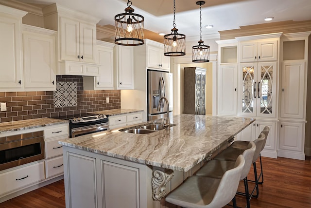 kitchen featuring a kitchen bar, stainless steel appliances, sink, decorative light fixtures, and an island with sink