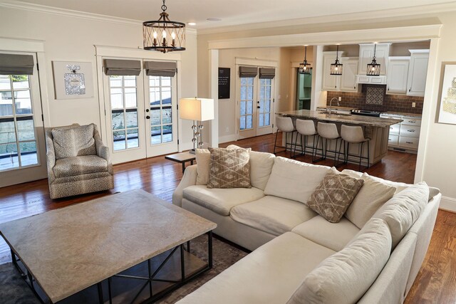 living room with french doors, an inviting chandelier, ornamental molding, and a healthy amount of sunlight