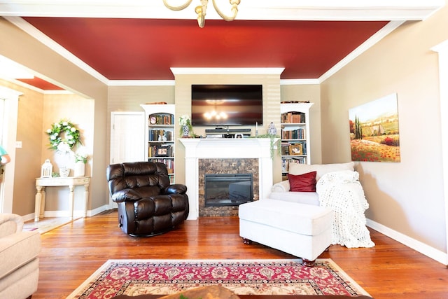 living room featuring hardwood / wood-style flooring, built in shelves, crown molding, and a tiled fireplace