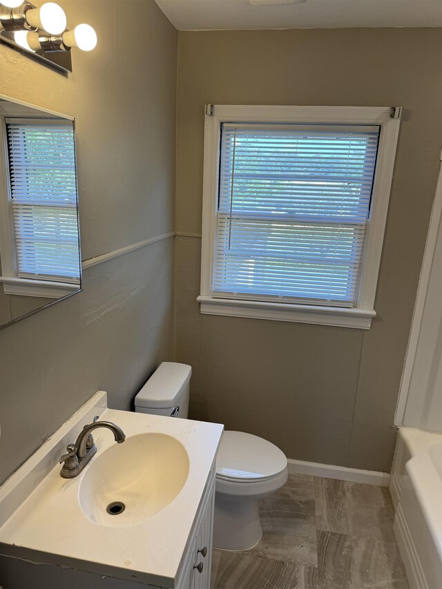  - bathroom with toilet, vanity, a tub to relax in, marble look tile flooring, and baseboards