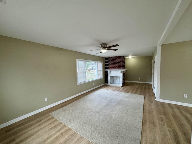 unfurnished living room featuring a ceiling fan, a fireplace, baseboards, and wood finished floors