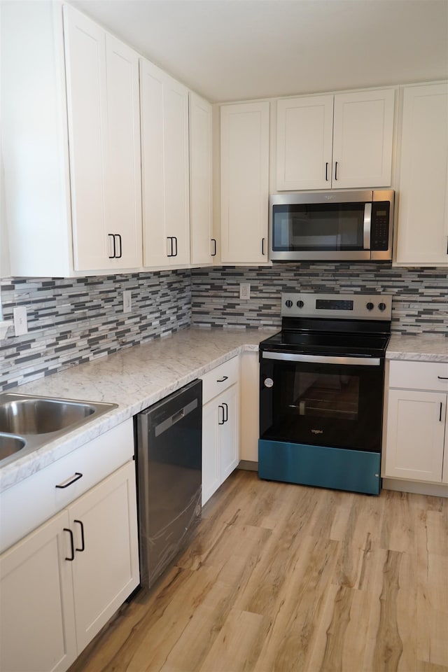 kitchen featuring decorative backsplash, white cabinetry, light wood-type flooring, and appliances with stainless steel finishes