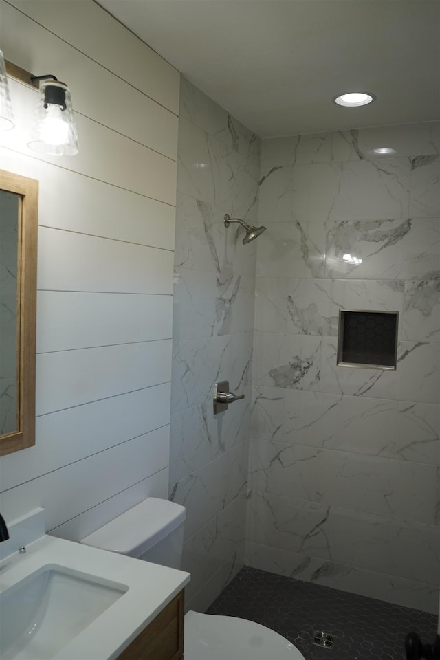 bathroom featuring tiled shower, vanity, toilet, and wooden walls