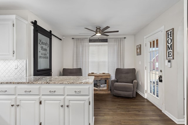 kitchen with ceiling fan, a barn door, dark wood-style flooring, white cabinets, and decorative backsplash