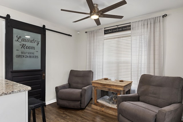 sitting room with ceiling fan, a barn door, dark wood-type flooring, and baseboards