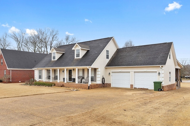 new england style home featuring covered porch, a garage, brick siding, dirt driveway, and stucco siding