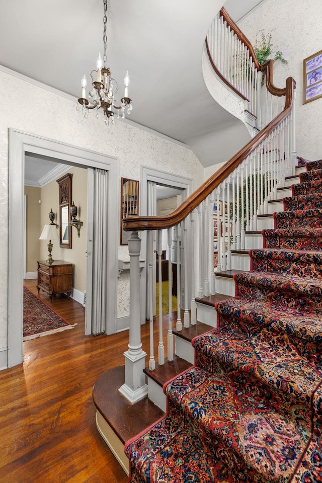 staircase featuring hardwood / wood-style floors, a notable chandelier, ornamental molding, and lofted ceiling