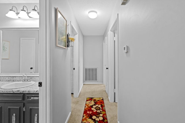 hallway featuring sink, a textured ceiling, and light carpet