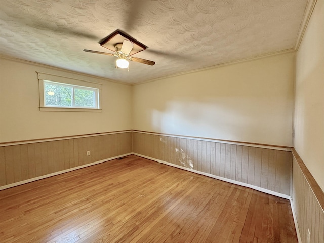  - spare room with wood-type flooring, a ceiling fan, a textured ceiling, wainscoting, and crown molding