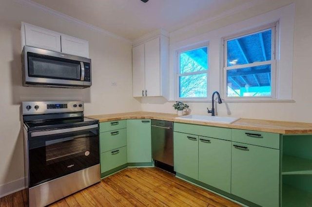  - kitchen featuring appliances with stainless steel finishes, green cabinets, light wood finished floors, wood counters, and ornamental molding