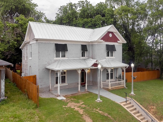  - view of front of house featuring metal roof, fence, a front lawn, and brick siding