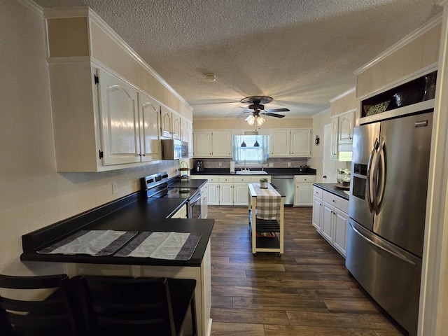  - kitchen featuring appliances with stainless steel finishes, crown molding, a ceiling fan, dark countertops, and a textured ceiling