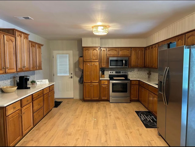  - kitchen with appliances with stainless steel finishes, light wood-type flooring, light countertops, and brown cabinets
