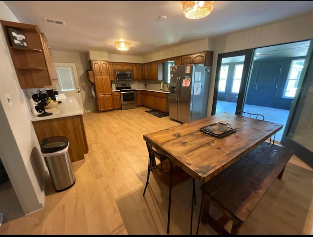  - kitchen featuring appliances with stainless steel finishes, open shelves, light countertops, and light wood finished floors