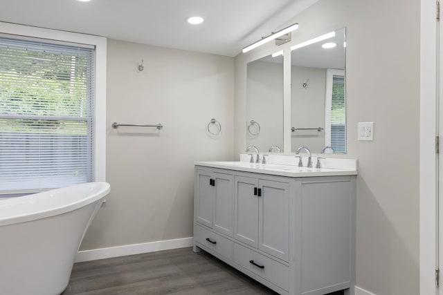  - full bath with double vanity, a soaking tub, baseboards, wood finished floors, and recessed lighting