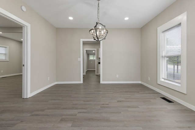  - unfurnished dining area featuring healthy amount of natural light, a chandelier, wood finished floors, and recessed lighting