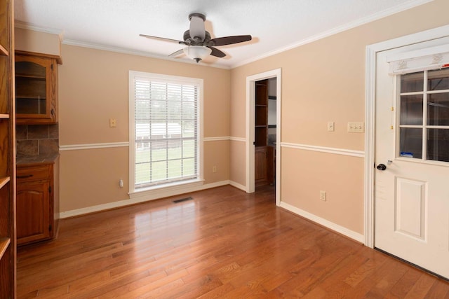 unfurnished room with wood finished floors, a ceiling fan, visible vents, and ornamental molding