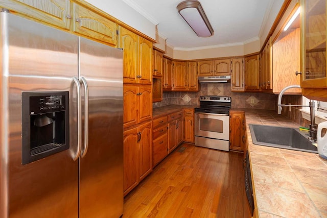kitchen featuring tile counters, under cabinet range hood, stainless steel appliances, a sink, and crown molding