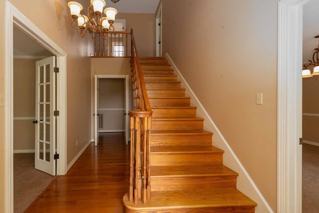 staircase with wood finished floors, baseboards, and an inviting chandelier