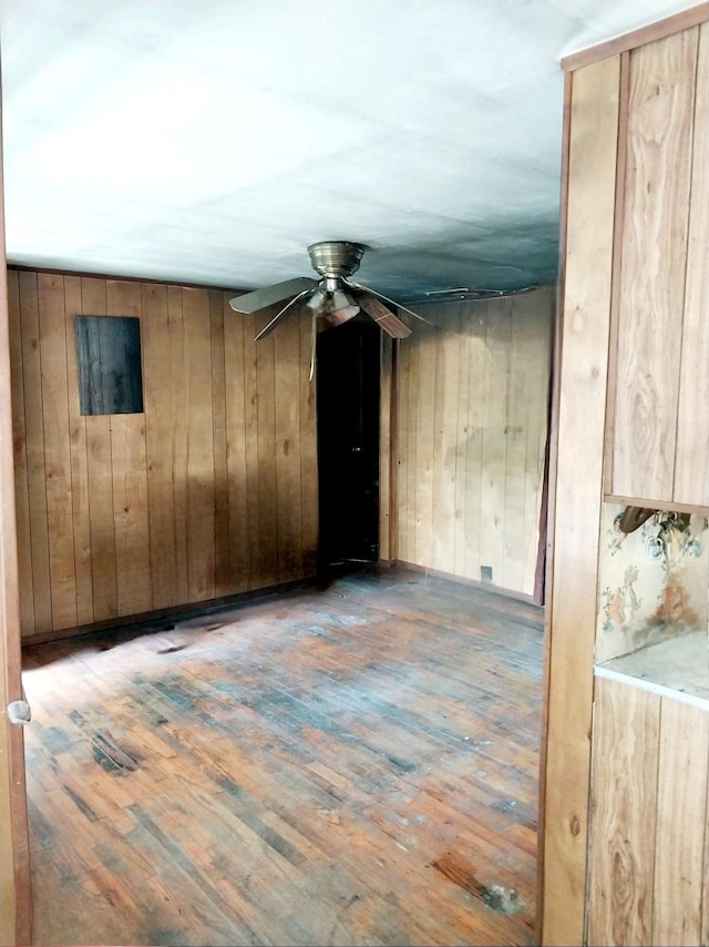 empty room with wood-type flooring, ceiling fan, and wooden walls