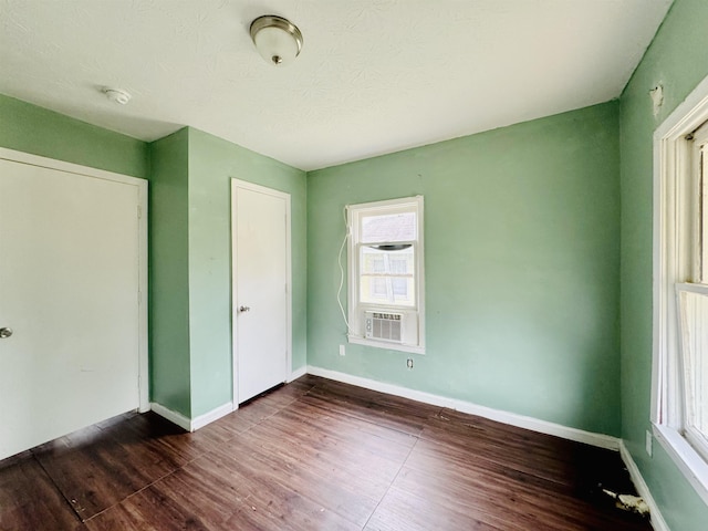 unfurnished bedroom featuring dark hardwood / wood-style flooring, a closet, multiple windows, and cooling unit