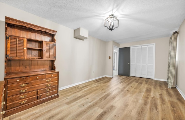 unfurnished bedroom with a chandelier, a closet, a textured ceiling, and light wood-type flooring