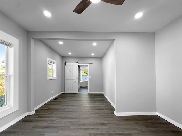 unfurnished room with a barn door, dark hardwood / wood-style floors, and ceiling fan