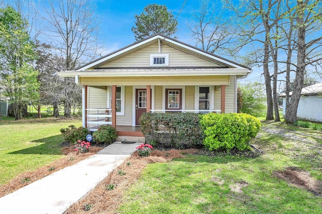 bungalow-style house featuring covered porch, metal roof, and a front lawn