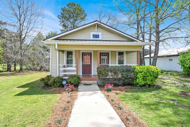 bungalow-style home featuring covered porch, metal roof, a standing seam roof, and a front lawn