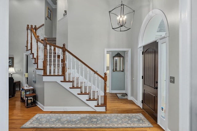 foyer with light wood-type flooring, a towering ceiling, and an inviting chandelier