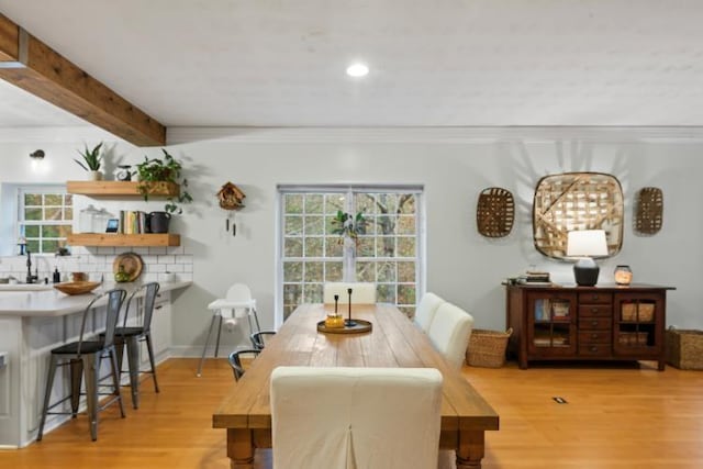 dining space featuring beam ceiling, ornamental molding, and light wood-type flooring