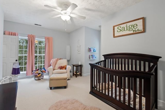 carpeted bedroom featuring ceiling fan, a textured ceiling, and a crib