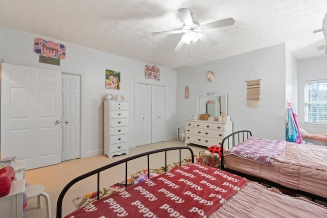 bedroom with multiple closets, ceiling fan, carpet, and a textured ceiling