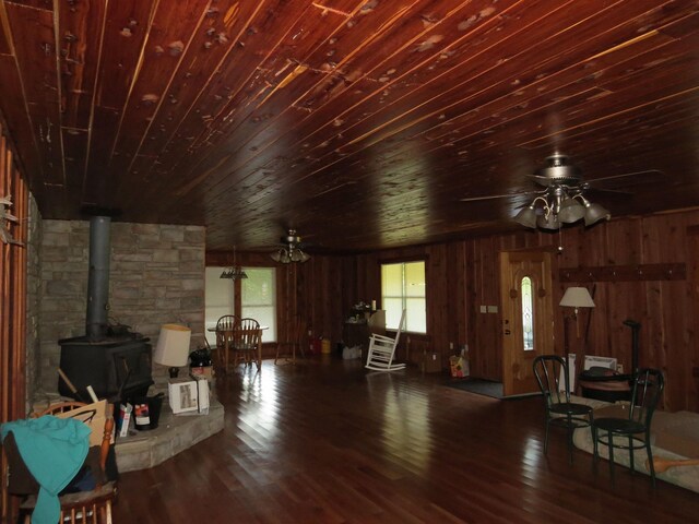 living room with ceiling fan, dark hardwood / wood-style floors, wood ceiling, and a wood stove