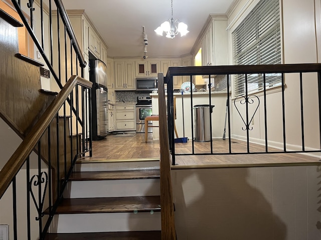  - stairway featuring a chandelier, wood finished floors, and track lighting