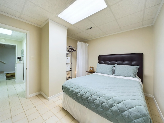 bedroom with a drop ceiling, ornamental molding, and light tile patterned flooring