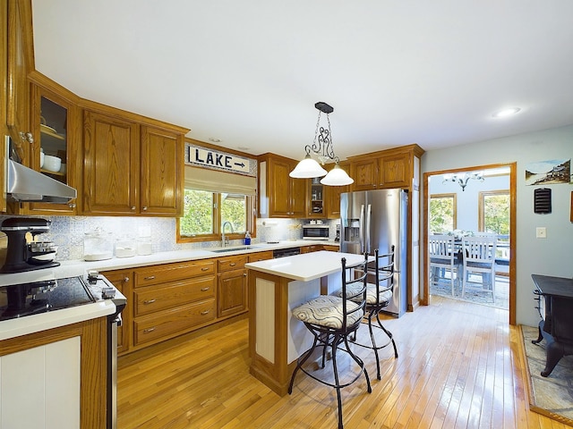 kitchen with sink, hanging light fixtures, stainless steel fridge with ice dispenser, a kitchen island, and light wood-type flooring